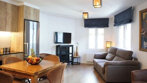 A modern living room with a wooden dining table, a sofa, and a TV on the wall. - Telecabine365  (La Massana)