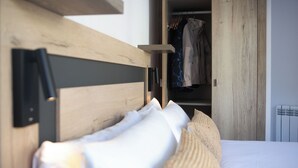 A bedroom with a wooden headboard, white bedding, and a visible closet with hanging clothes. - Telecabine365  (La Massana)