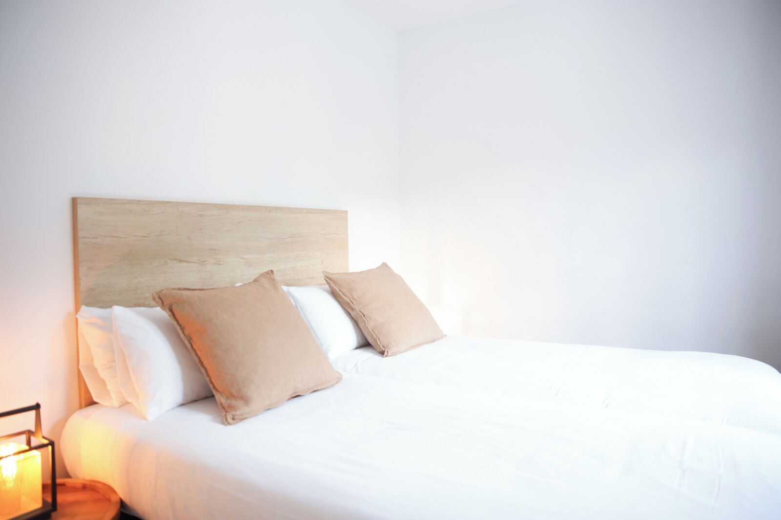 Uma cama bem arrumada com cabeceira de madeira, duas almofadas bege e edredom branco.