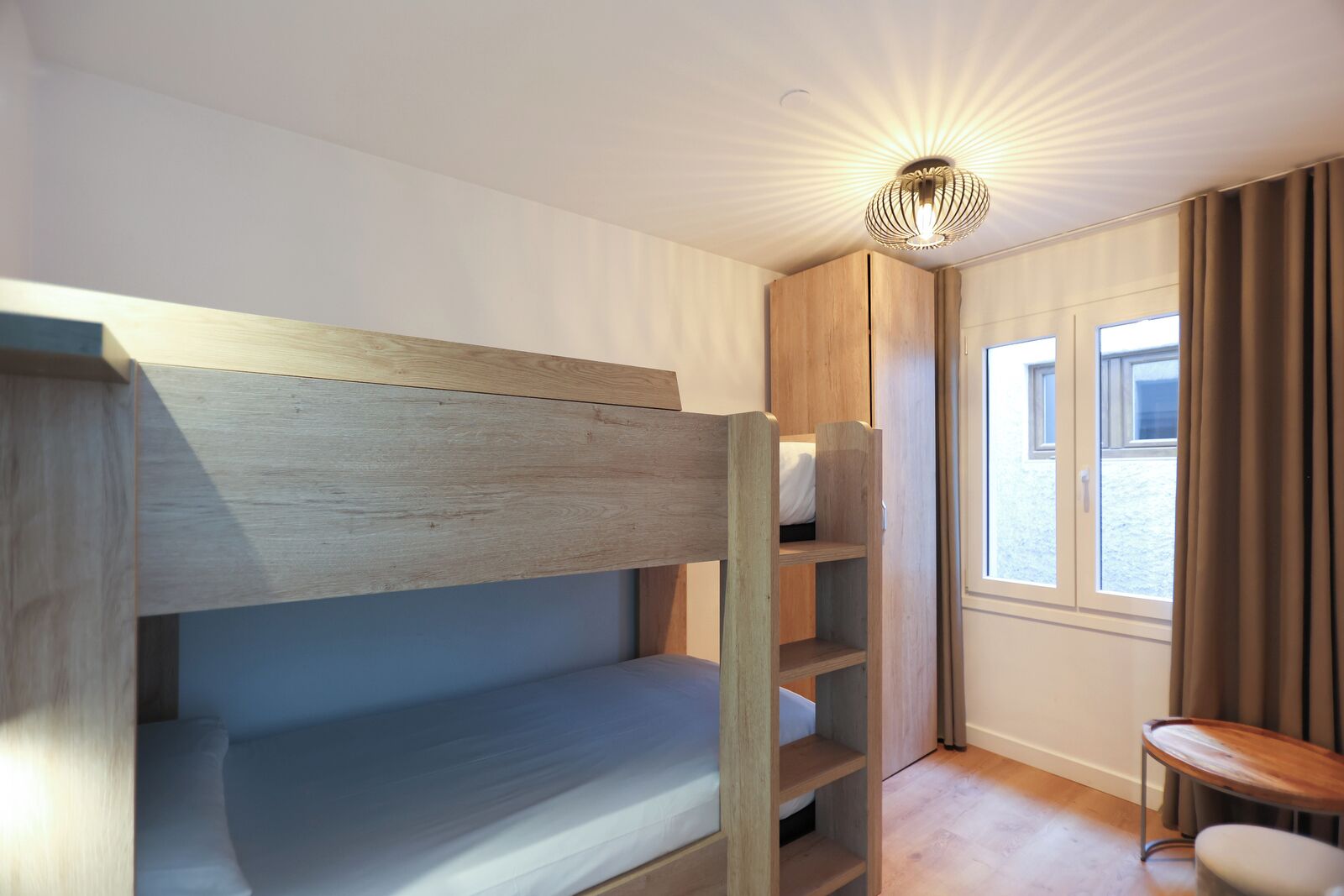 A bunk bed room with a wooden headboard, a built-in wardrobe, and a window with curtains.