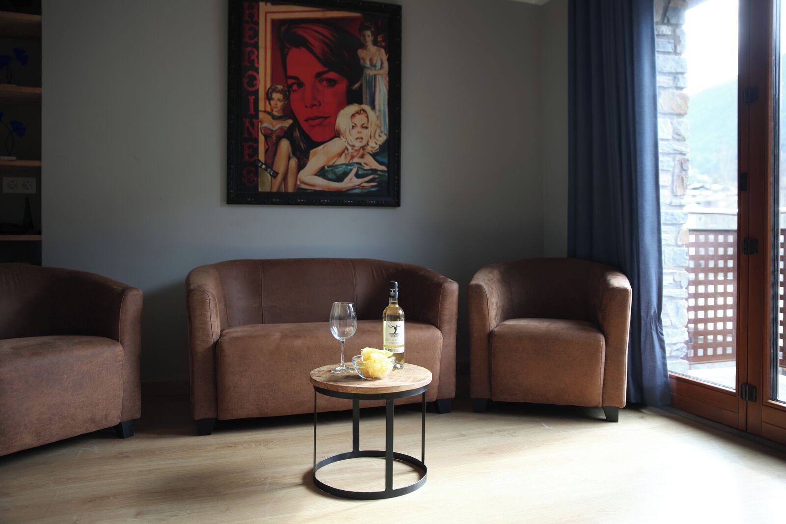 A living room with three brown leather sofas, a small round table with a wine bottle and a glass, and a painting on the wall.
