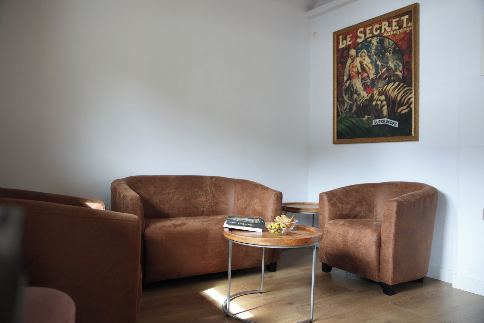 A living room with two brown sofas, a small wooden coffee table with a book and snacks, and a poster on the wall.