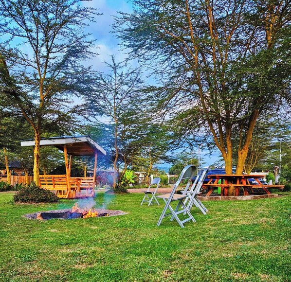 A grassy outdoor area with a fire pit, picnic tables, and a covered seating area.