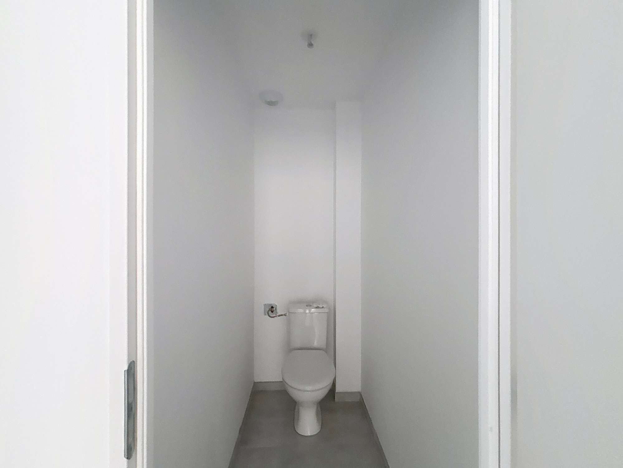 Pieni, valkoinen ja kapea kylpyhuone, jossa on wc-istuin ja näkyvillä oleva wc-paperiteline.