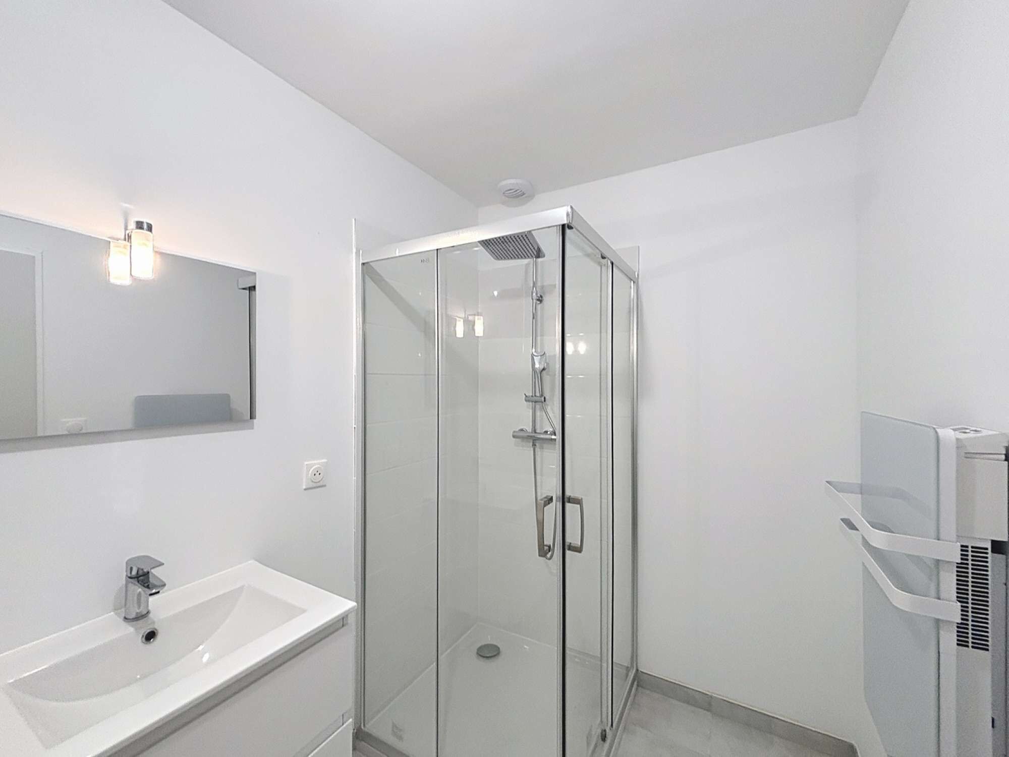 A modern bathroom with a glass-enclosed shower, a white sink, and a mirror with wall-mounted lights.