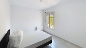 Ein schlicht eingerichtetes Schlafzimmer mit Bett, Fenster und Heizkörper.