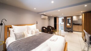 A hotel room with a large bed, a sitting area with chairs, a small table, and a kitchenette in the background. - Urban Getaway: Maillol Suite in the Center with Free Wifi (Perpignan)