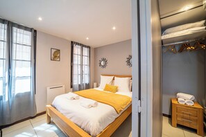 Ein Schlafzimmer mit einem Bett, einem Nachttisch mit Handtüchern, einem Heizkörper und einem Kleiderschrank mit Kleidung.