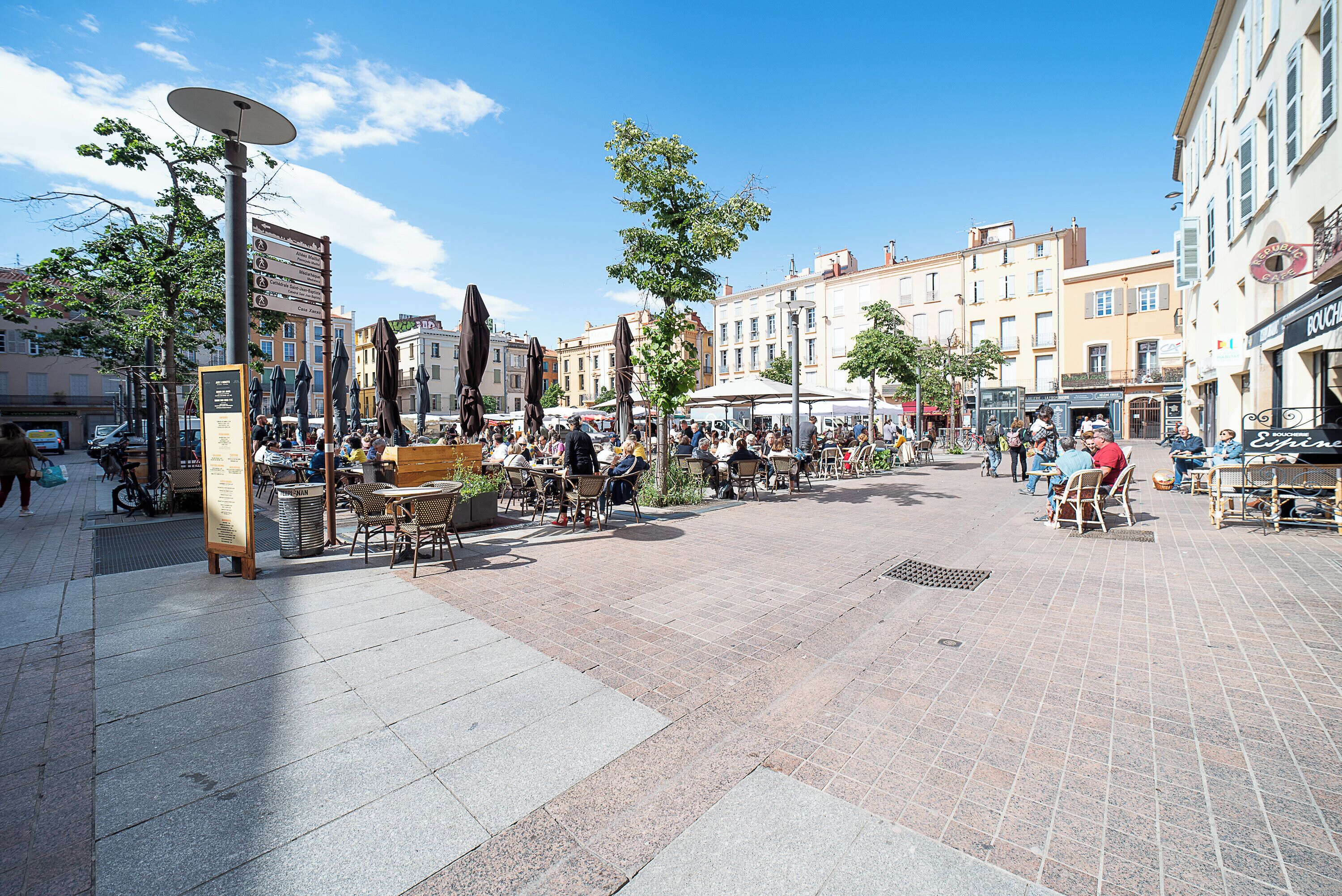 An outdoor public square with seating areas, a central fountain, and surrounding buildings.