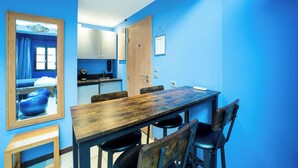 Una habitación con una mesa de comedor de madera, cuatro sillas, un espejo, una pared azul y una puerta que da a una cocina.