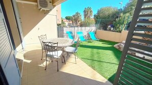 A patio with a round table and chairs, a small lawn, and a wooden fence. - Apartment with Pool, Air Conditioning, WiFi, and Garage (Collioure)