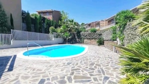 A swimming pool with a stone tiled deck, surrounded by greenery and a white fence. - Apartment with Pool, Air Conditioning, WiFi, and Garage (Collioure)