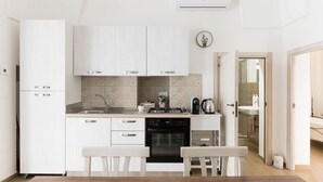 Una cocina compacta con armarios blancos, lavavajillas, estufa y pileta. Hay un pequeño comedor con dos sillas y un banco.