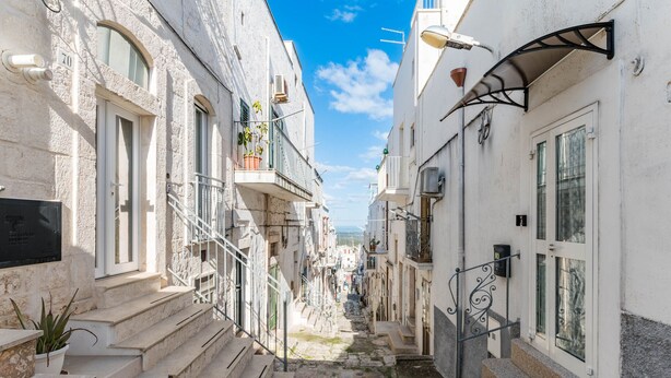 Una calle estrecha flanqueada por edificios, con escalones que conducen a la entrada y un cielo despejado.