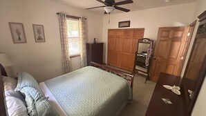 Ein Schlafzimmer mit Bett, Kleiderschrank, Spiegel und Deckenventilator.