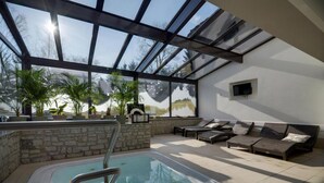 A modern indoor pool area with a glass ceiling, stone walls, and a comfortable seating area with cushions. - Rezydencja nad Wodospadem Spa&Wellness (Jelenia Gora)