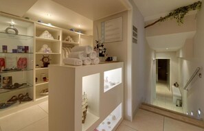 A hotel lobby with a reception desk, glass display cases, shelves with towels and toiletries, and a staircase leading to other areas. - Rezydencja nad Wodospadem Spa&Wellness (Jelenia Gora)