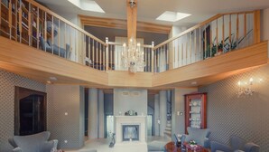 A spacious living area with a high ceiling, a chandelier, a fireplace, and a dining table with chairs. - Rezydencja nad Wodospadem Spa&Wellness (Jelenia Gora)