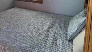 Une petite chambre avec un lit simple et une grande fenêtre donnant sur une terrasse et les montagnes.