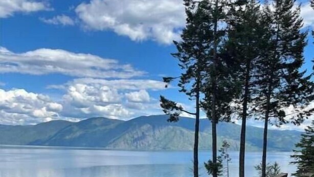 Une terrasse en bois avec un banc donnant sur un lac paisible et des montagnes.