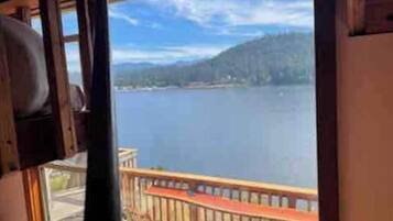 Vue depuis une chambre dont la fenêtre donne sur un lac et une terrasse en bois.