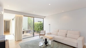 Una sala de estar moderna con una mesa de centro de vidrio, un sofá y un televisor sobre un mueble de madera.