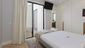 Un dormitorio moderno con una cama grande, un ventanal corredero que da a un balcón, un televisor de pantalla plana montado en la pared y un diseño minimalista.