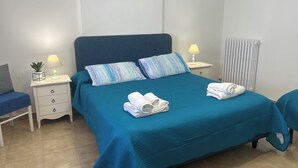 A neatly made bed with blue bedding and pillows, two bedside lamps, a small potted plant, and a folded towel on the bed. - Cozy house with veranda (Otranto)