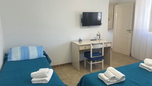A hotel room with two beds, a desk, a chair, a TV, and a door. - Cozy house with veranda (Otranto)