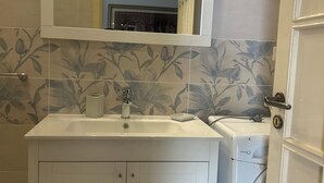 A bathroom with a white sink, a mirror above it, and a washing machine to the right. - Cozy house with veranda (Otranto)