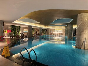 An indoor swimming pool with clear water, surrounded by lounge chairs and a bar area. - Alacarte Ha Long Bay By Azure (Bai Chay)