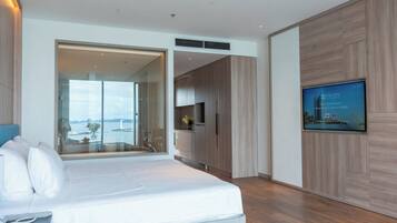 A modern hotel room with a large bed, a TV, and a view of the sea.