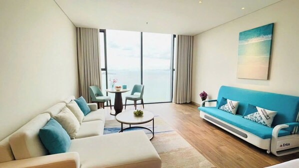A modern living room with a sofa, chairs, a coffee table, and a view of the sea through large windows. - Alacarte Ha Long Bay By Azure (Bai Chay)