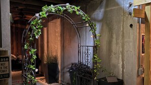 Een binnentuin met een houten boog, plantenpotten en een metalen poort.