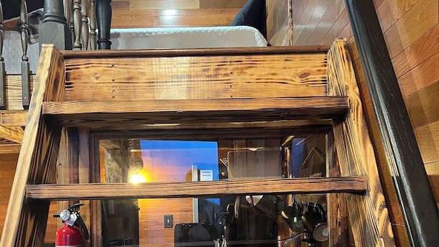 Een houten trap met een glazen paneel, leidend naar een kamer met uitzicht op een ondergaande zon.