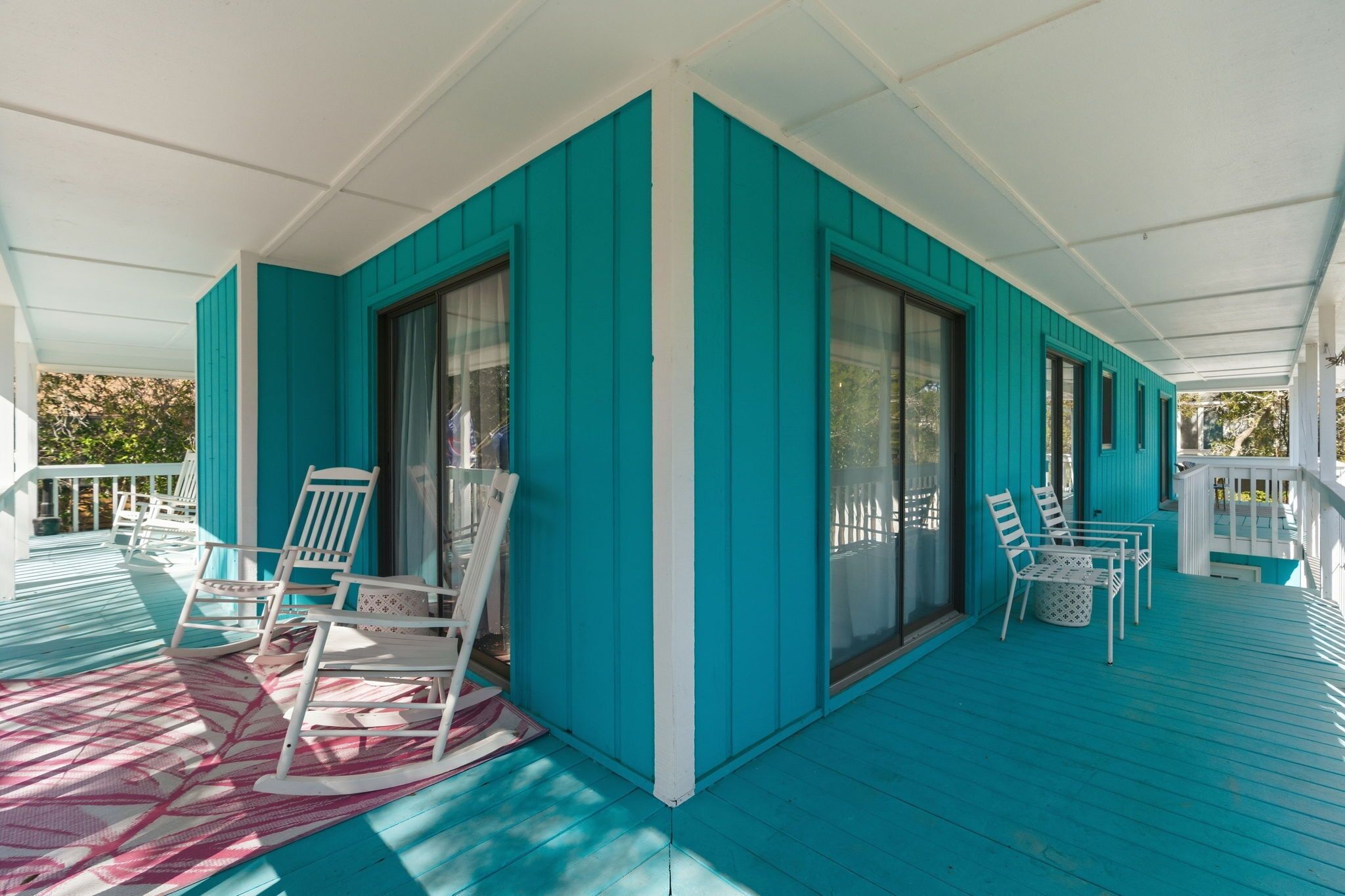A covered porch with teal siding, white railings, and a patterned rug.