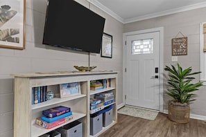 Ein Zimmer mit einem an der Wand befestigten Fernseher, einem Bücherregal mit Spielen, einer Tür mit Fenster und einem Schild an der Wand.
