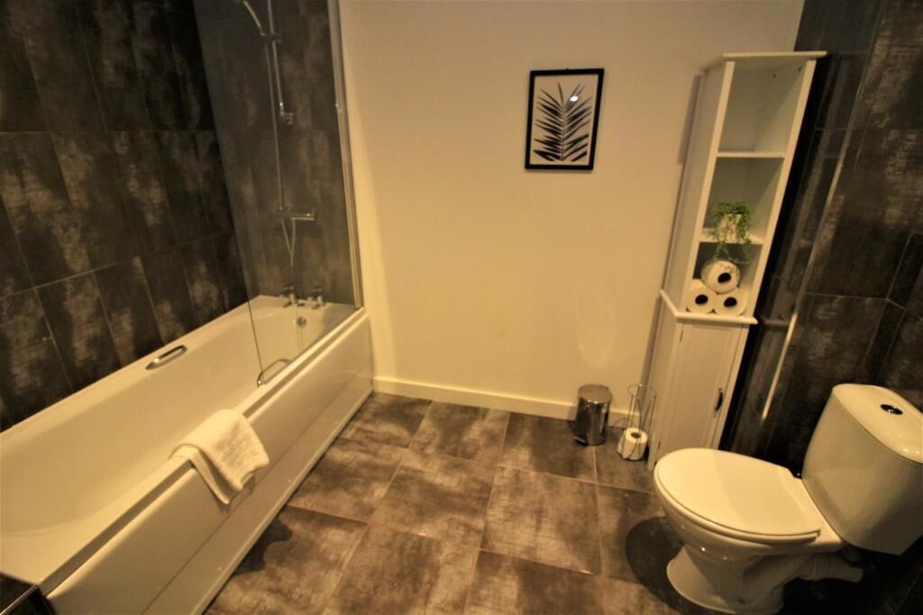 A bathroom with a bathtub, toilet, and a shelf with toiletries.
