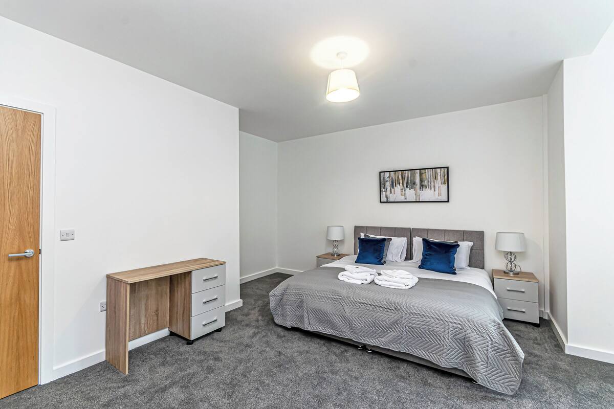 A bedroom with a bed, bedside tables, a desk, and a door.