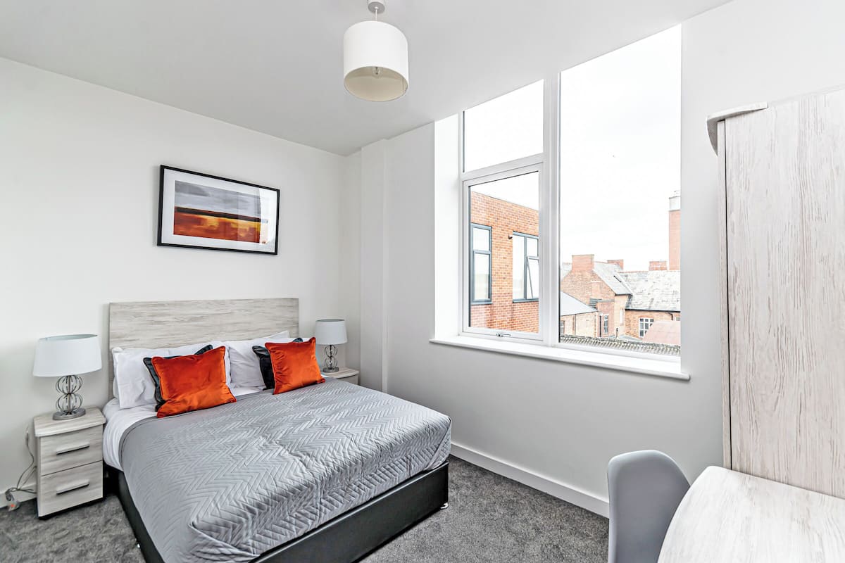 A modern bedroom with a bed, two bedside tables, a window, and a view of buildings.