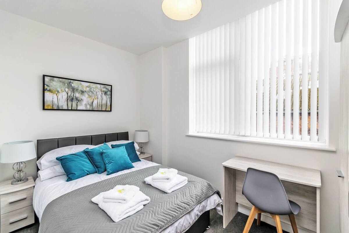 A modern hotel room with a bed, a desk, and a window with blinds.