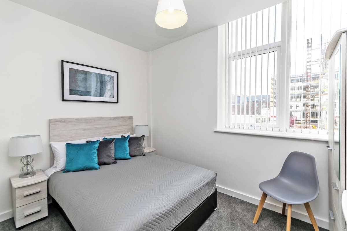 A modern bedroom with a bed, bedside tables, a chair, and a window with a view of buildings.