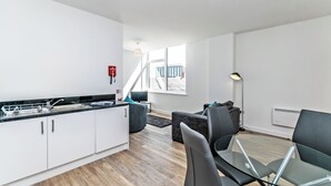 A modern kitchen with white cabinets, a black countertop, and a dining area with a glass table and chairs. - City Suites by Guestz (Chester)