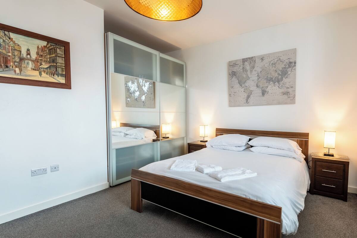 A neatly arranged hotel room with a large bed, bedside tables, a wardrobe, and a world map on the wall.
