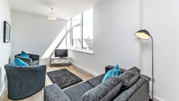 A modern living room with grey sofas, a black rug, a TV, and a lamp. - City Suites by Guestz (Chester)