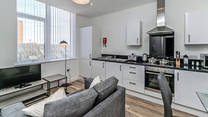 A modern kitchen with white cabinets, a stainless steel range hood, and a black countertop. - City Suites by Guestz (Chester)
