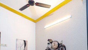 A dining area with a wooden table and chairs, a ceiling fan, a wall-mounted bicycle clock, and a framed abstract painting.