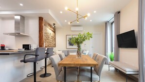 Eine moderne Küche mit Holztisch, Barhocker, einer Wand aus Stein und einem großen Fenster mit Vorhängen.