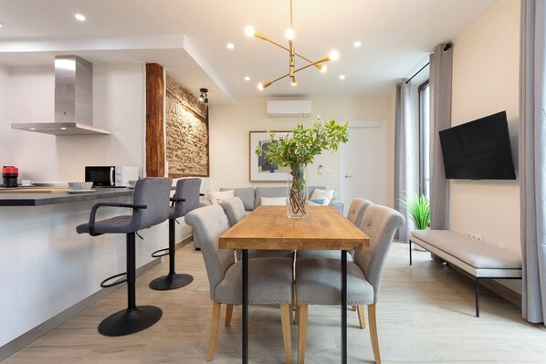 A modern kitchen with a wooden table and bar stools, a stone accent wall, and a large window with curtains. - Genteel Home Plaza del Realejo (Granada)