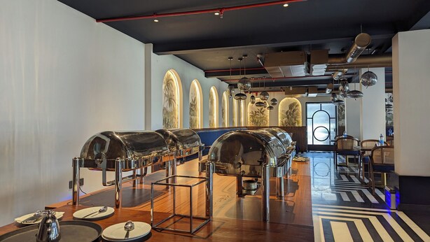 A modern restaurant interior with a long counter, metal serving stations, and a patterned floor.